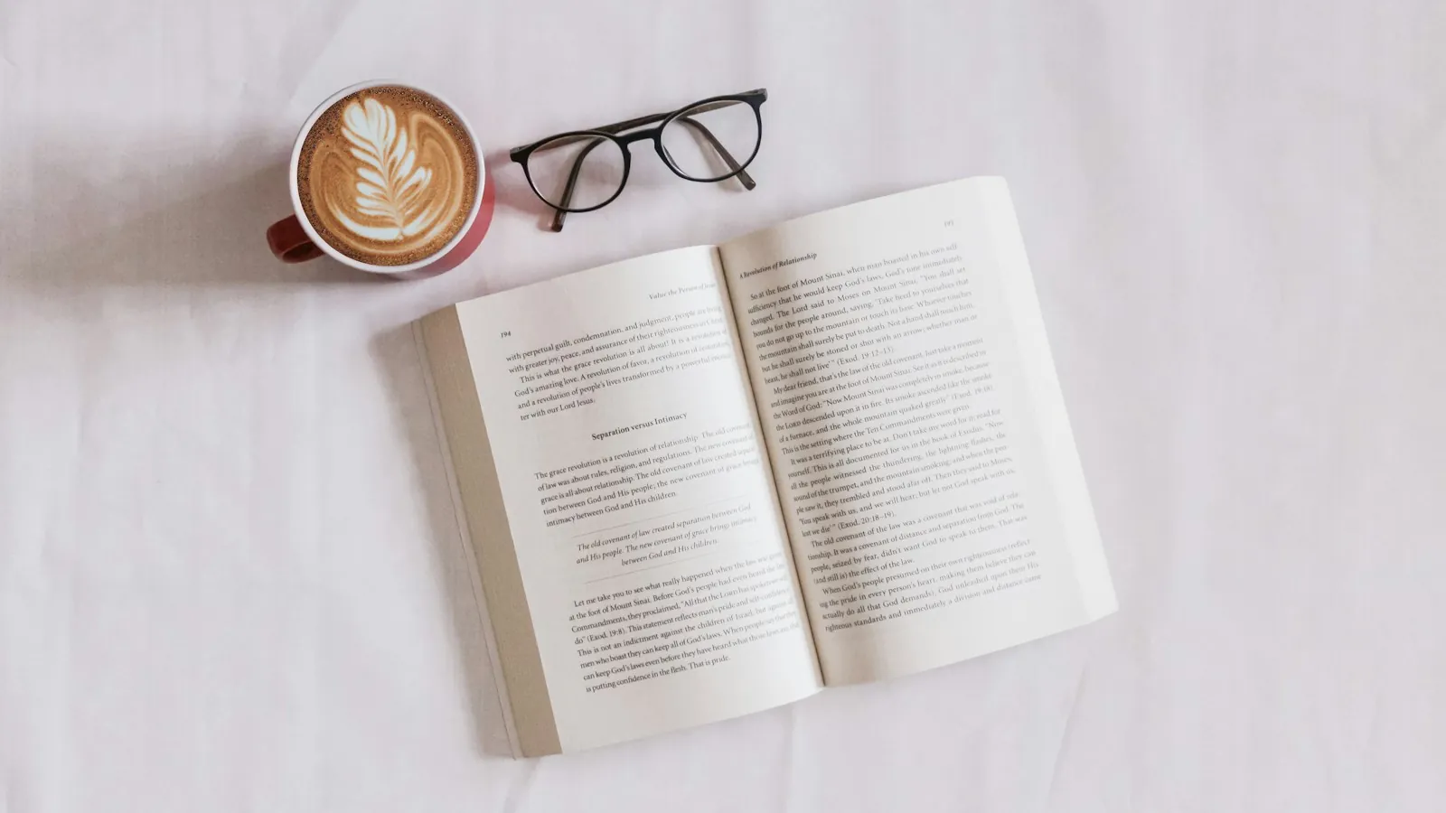 Un libro abierto junto a una taza de café y unas gafas