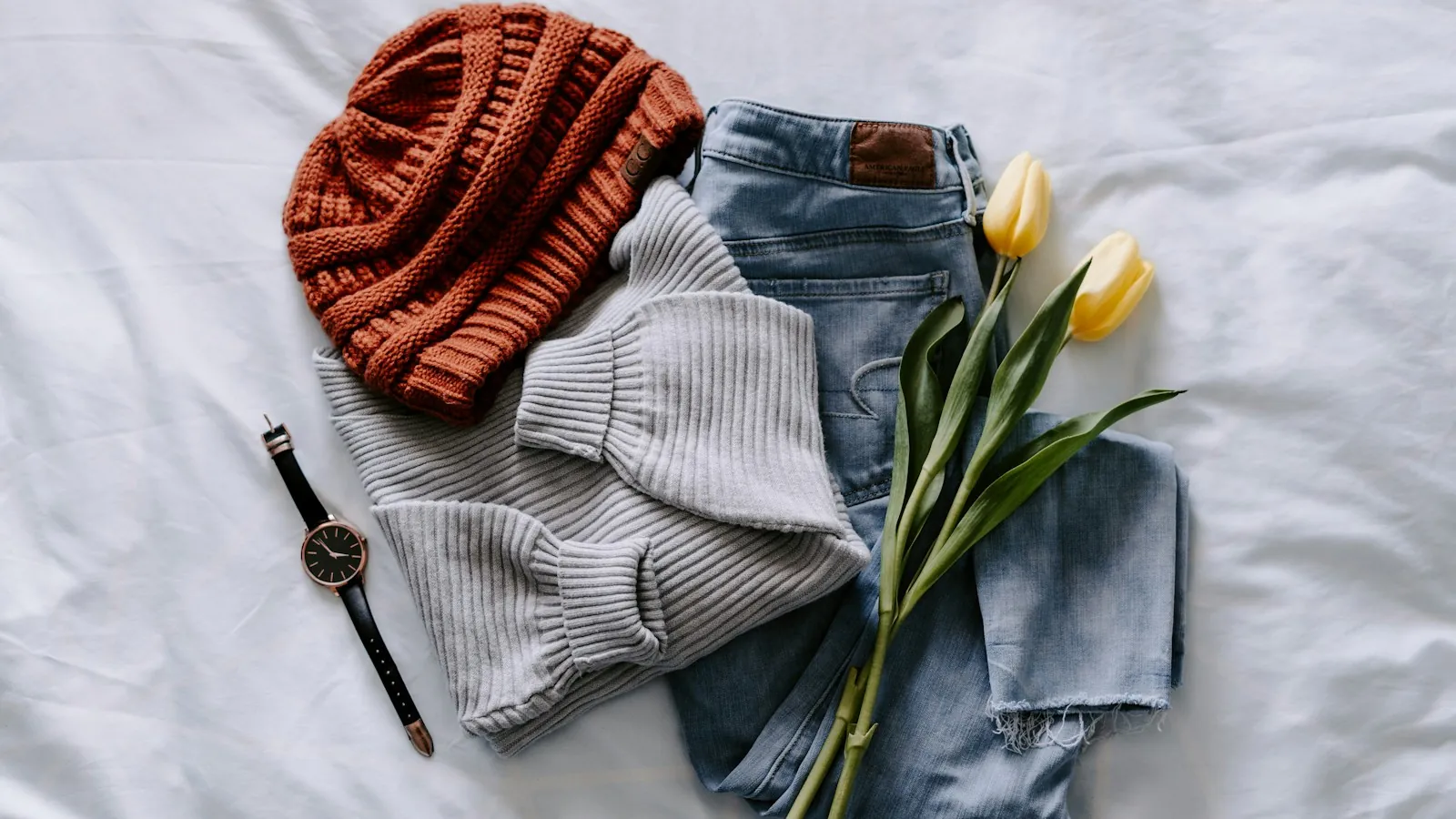 A knitted jumper, a beanie and jeans laid out flat